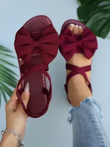 Nahaufnahme weinroter flacher Sandalen mit großer Stoffschleife und elastischen Kreuzgurten