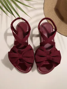 Detailaufnahme burgunderfarbener flacher Sandalen mit großer Schleife und elastischen Riemen