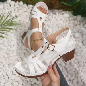 Elegant white chunky heel sandals with T-strap and peep-toe design on white pebbles.