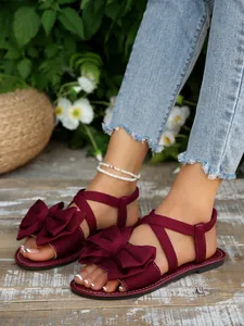 Modische burgunderrote flache Sandalen mit großer Schleife auf Holzgartenboden