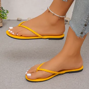 Close-up detail of women's bright yellow braided strap thong flip-flops on feet.