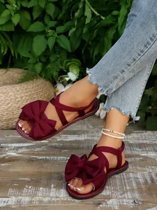 Detailansicht eleganter burgunderroter flacher Sandalen mit großer Schleife und Knöchelriemen