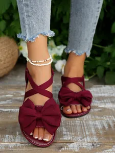 Nahaufnahme weinroter flacher Sandalen mit übergroßen Schleifen und Perlenfußkettchen.