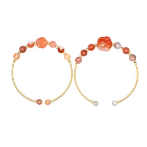 Detail von zwei vergoldeten Armbändern mit roten Achatperlen und Katzenpfoten-Anhänger