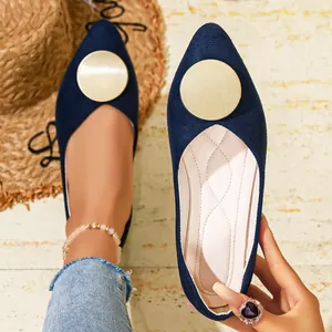 Detalle de mano sujetando zapato plano azul marino con adorno dorado circular y punta afilada