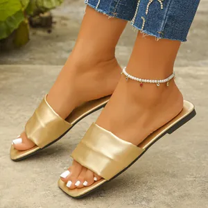Close-up of golden metallic flat slides with square toe and wide padded strap