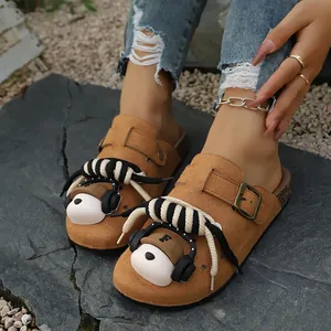 Close-up detail of camel suede clogs featuring 3D bear accessories and rope trim