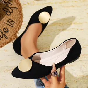 Vista detallada de un zapato plano negro de punta con un gran adorno de disco de metal dorado