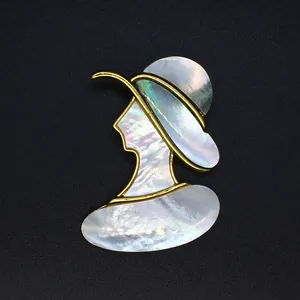 Détail d'une broche en nacre irisée avec une silhouette de femme dans un cadre doré.