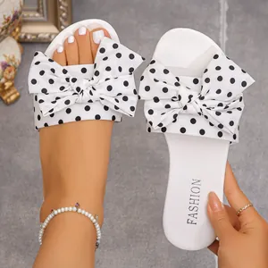 Detail view of white flat sandals featuring a large polka dot bow and FASHION footbed