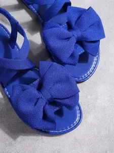 Detailaufnahme von blauen flachen Sandalen mit großer Stoffschleife und weißen Nähten