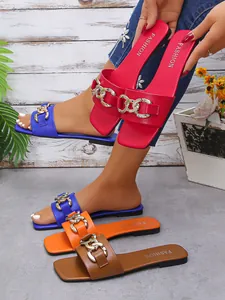 Close-up of stylish women's square toe flat slides in multiple colors with gold chains.