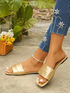 Close-up of golden square-toe flat slides worn in a stylish outdoor setting