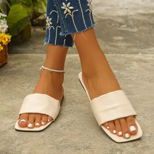 Detailed view of cream square toe flat slide sandals on feet with white nail polish
