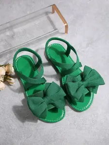 Detailansicht grüner flacher Sandalen mit einer großen Schleife aus Textilgewebe.