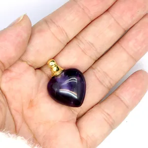 Dettaglio di un ciondolo a forma di cuore in ametista per oli essenziali tenuto nel palmo.