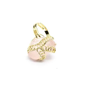 Dettaglio di un anello in filo d'oro avvolto a mano con una pietra di cristallo rosa grezzo.