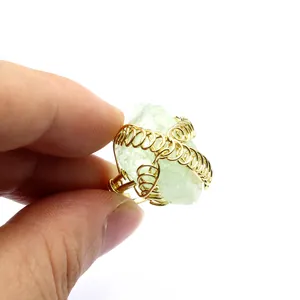 Primo piano di un anello artigianale in filo dorato con una pietra di cristallo verde grezzo