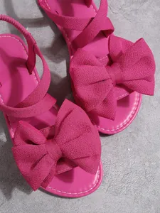 Detailaufnahme von pinkfarbenen flachen Sandalen mit großen strukturierten Stoffschleifen