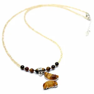 Close-up detail of tiger eye butterfly pendant on a beaded necklace with golden hues.