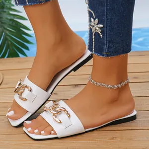 Close-up detail of white square-toe flat sandals featuring a stylish gold chain link accent