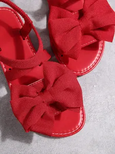 Detailaufnahme einer leuchtend roten Schleifendekoration auf flachen, offenen Sandalen