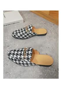 Close-up of men's houndstooth mules with gold metal chain buckle detail on stone floor.