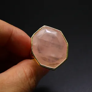 Gros plan d'une grande bague octogonale en quartz rose avec monture dorée sur fond noir.