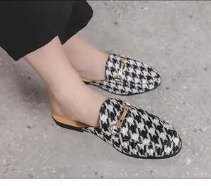 Detail view of men's houndstooth mules with gold buckle on gray stone floor.