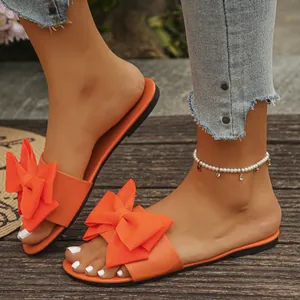 Eleganti ciabatte piatte arancioni da donna con un grande fiocco decorativo in tessuto
