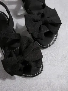Nahaufnahme schwarzer flacher Sandalen mit übergroßen schimmernden Schleifen
