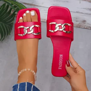 Close-up detail of red square-toe flat slide sandals with chunky gold chain decoration.