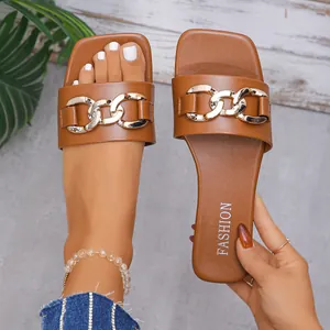 Detailed view of women's brown square toe flat sandals with gold chain, shown on foot