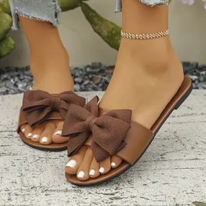 Dettaglio di sandali piatti marroni con grande fiocco in tessuto indossati da una modella