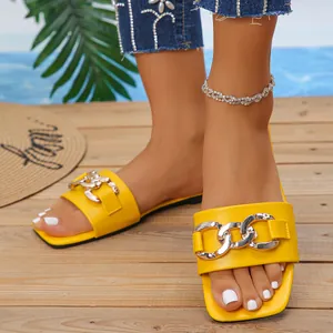 Close-up of yellow square toe flat sandals with decorative silver chain link on wooden deck.