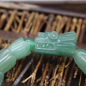Detaillierte Makroansicht eines geschnitzten grünen Naturstein Drachenkopf Armbands für Herren.