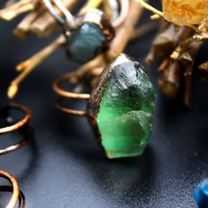 Dettaglio macro di una gemma di cristallo verde grezzo incastonata in un anello di rame.