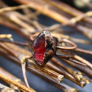 Primo piano di una pietra preziosa rossa grezza incastonata in un anello di rame retrò