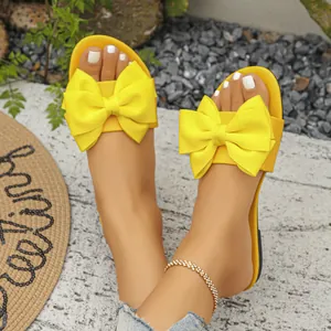 Primo piano di sandali bassi gialli con grande fiocco sui piedi di una modella.