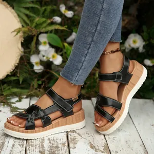 Close-up of black Roman wedge sandals with thick wood-grain soles on a wooden deck