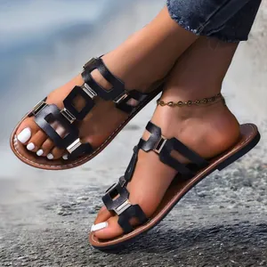 Gros plan de sandales plates noires chics avec boucles dorées sur fond extérieur stylé.