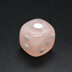 Primer plano detallado de un dado de piedra natural rosa con puntos sobre fondo negro