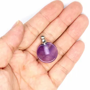 Gros plan d'un pendentif flacon de parfum en améthyste naturelle tenu dans la main.