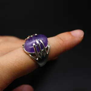 Detail view of a purple natural stone ring held by a silver-colored hand-shaped claw.