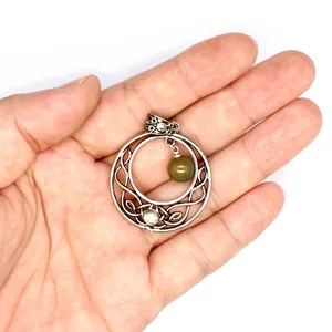 Close-up view of a vintage silver Celtic moon pendant with a green bead held in hand