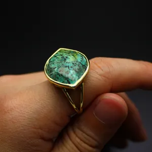Macro shot of a faceted green turquoise stone ring with a golden split shank on a finger.