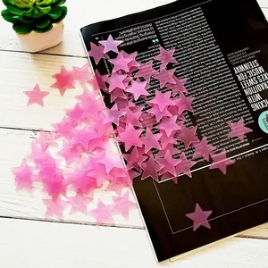 Close-up of pink glow-in-the-dark star stickers scattered on a magazine and wooden table.
