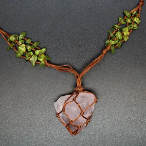 Detail of a handmade rose quartz pendant necklace in a brown woven net with peridot stones.