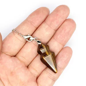 Close-up of a hexagonal tiger eye stone pendulum held in hand on white background.