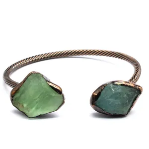 Macro view of retro twisted metal cuff bracelet featuring two natural green crystal stones.